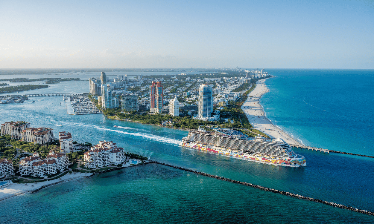 Kreuzfahrtschiff der Norwegian Cruise Line fährt aus dem Hafen von Miami, umgeben von Hochhäusern und Stränden.
